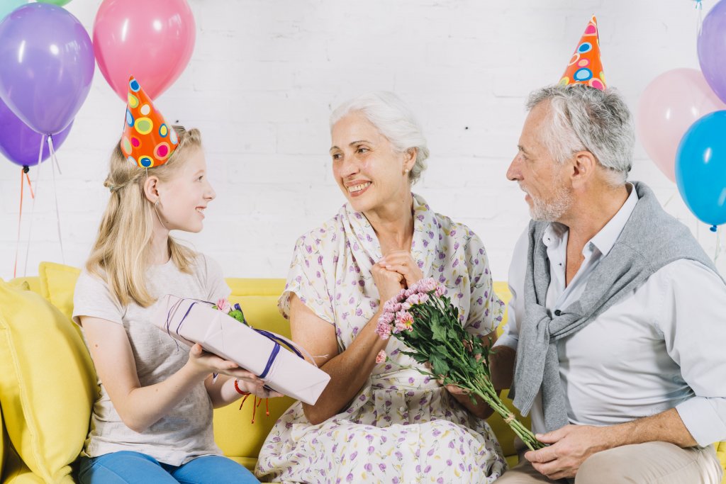 husband-and-granddaughter-giving-birthday-gift-to-happy-woman.jpg